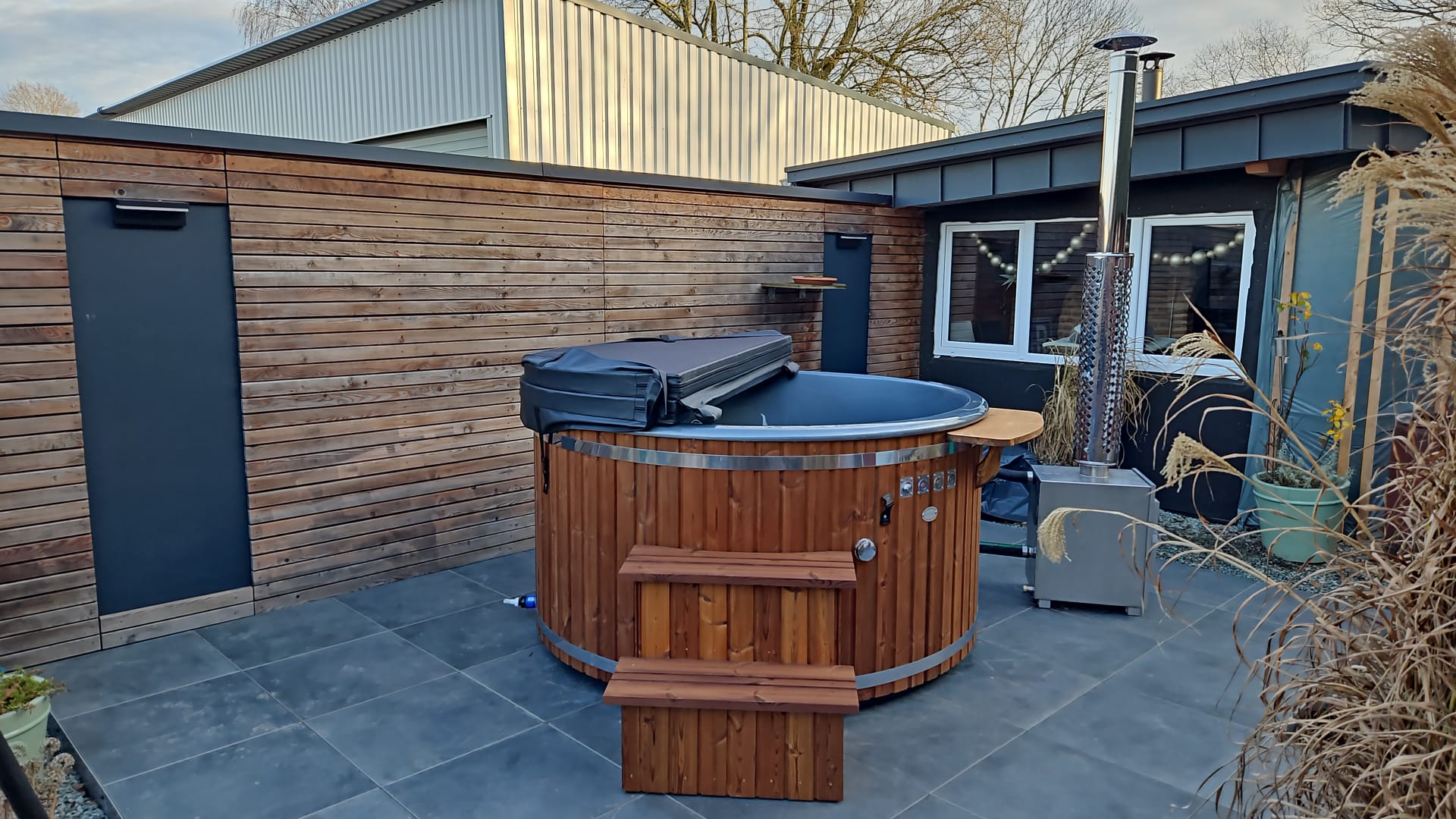 Runder Hot Tub aus Holz mit Holzofen und Einstiegsstufen auf einer Terrasse